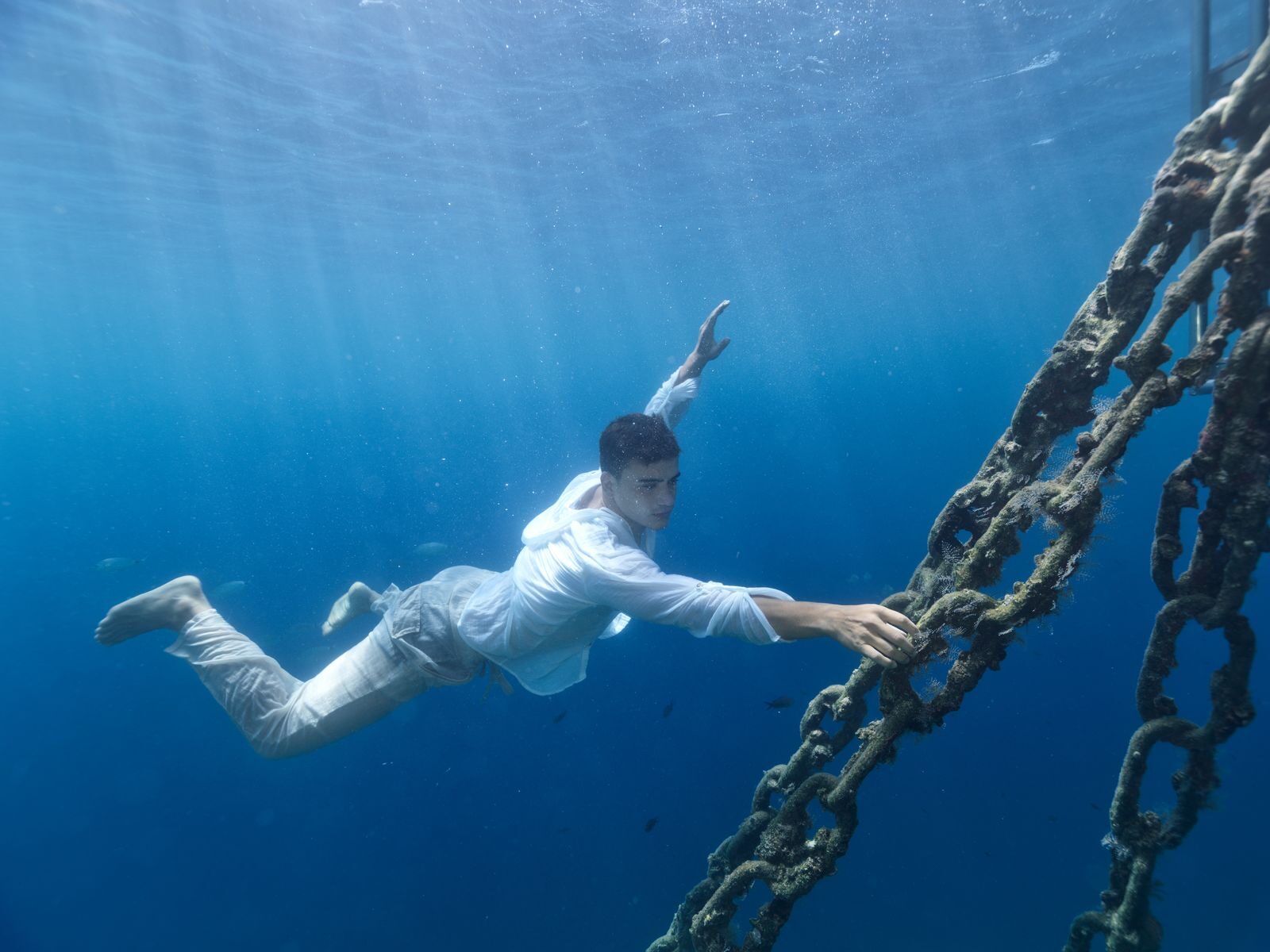 Man diving underwater holding a chain in Muğla, Turkey's clear sea.